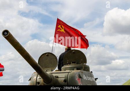 Russischer Panzer, der den Hammer und die Sichelrote Flagge fliegt. T-34-Panzer des zweiten Weltkriegs bei einer militärischen Nachstellung in Essex, Großbritannien. Rote Flagge fliegt Stockfoto