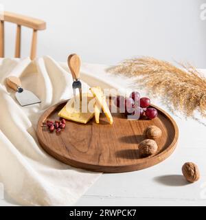 Traditionelle handgemachte Käseplatte aus Holz mit Walnüssen und Trauben auf dem Tisch Stockfoto