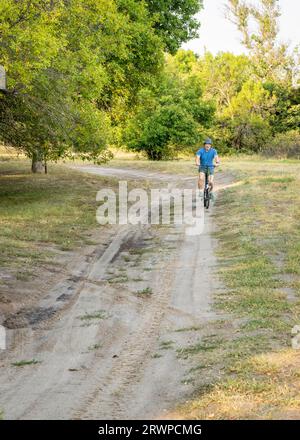 Der sportliche Senior man fährt ein Klappfahrrad auf einer Sandstraße im Wald auf dem Whitetail Campground im Nebraska National Forest Stockfoto