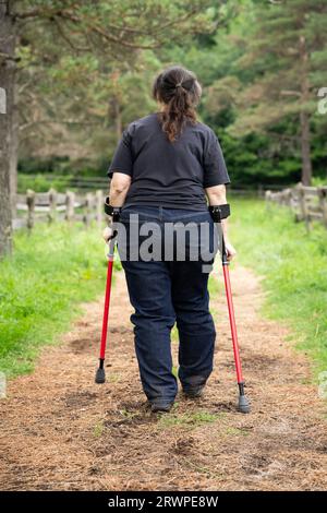 Eine behinderte Frau mit Unterarmkrücken, die auf einem Pfad spaziert Stockfoto