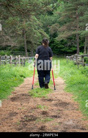 Eine behinderte Frau mit Unterarmkrücken, die auf einem Pfad spaziert Stockfoto