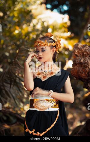 Stammeskönigin im Make-up, während sie eine goldene Krone und eine goldene Halskette mit dem schwarzen Kleid im Wald trägt Stockfoto