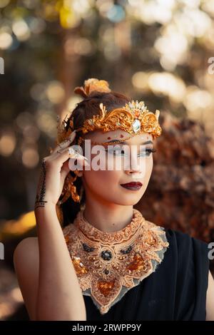 Stammeskönigin im Make-up, während sie eine goldene Krone und eine goldene Halskette mit dem schwarzen Kleid im Wald trägt Stockfoto