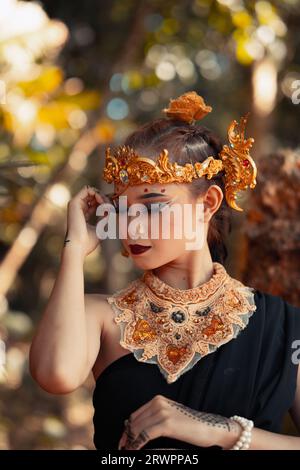 Stammeskönigin im Make-up, während sie eine goldene Krone und eine goldene Halskette mit dem schwarzen Kleid im Wald trägt Stockfoto