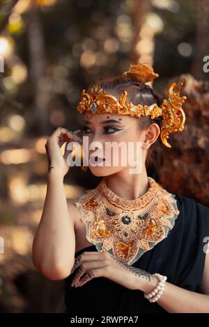 Stammeskönigin im Make-up, während sie eine goldene Krone und eine goldene Halskette mit dem schwarzen Kleid im Wald trägt Stockfoto