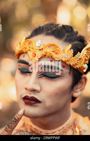 Asiatischer Mann mit einem denkenden Ausdruck, während er eine goldene Krone und eine goldene Halskette am Körper im Dschungel trägt Stockfoto
