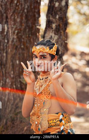 Balinesischer Mann, der im Wald steht, während er bei Tageslicht eine goldene Krone und eine goldene Halskette trägt Stockfoto