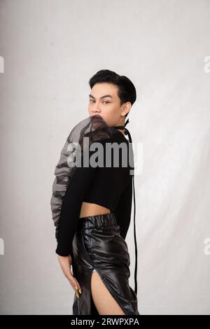 Asiatischer Mann posiert in einem schwarzen Kostüm, während er im Studio Make-up und schwarze Haare trägt Stockfoto