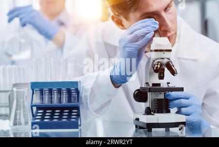 Junger Wissenschaftler oder Forscher in Arbeitsschutzkleidung studiert neues Virus im Mikroskop, um Gegenmittel zur Bekämpfung des Coronavirus zu entwickeln Stockfoto