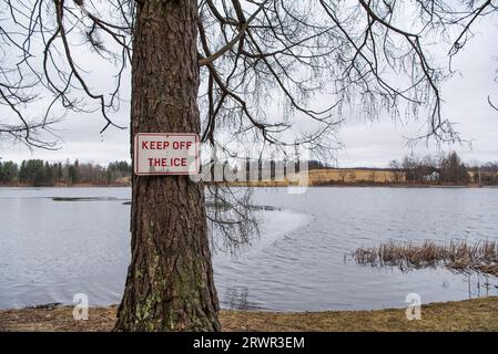 Ein Schild mit der Aufschrift „Keep off Ice“ auf einem einzelnen Baum am Rande des Wassers im Taconic State Park, Rudd Pond, in millerton, New york. Stockfoto