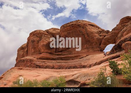 Frau klettert einen kleinen roten Bogen am Arches Nationalpark Stockfoto