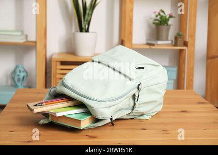 Stilvoller Schulrucksack mit Schreibwaren auf Holztisch im Wohnzimmer Stockfoto