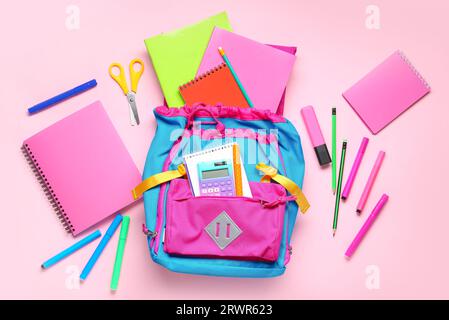 Stylischer Schulrucksack mit verschiedenen Schreibwaren auf rosafarbenem Hintergrund Stockfoto