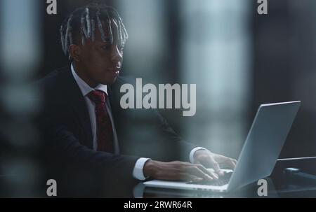 Fokussierter dunkelhäutiger Geschäftsmann sitzt an einem Tisch in einem modernen Büro und verwendet ein Notebook Stockfoto