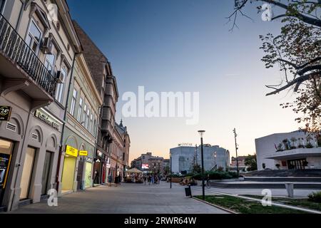 Bild von Menschen, die an der Fußgängerzone des Pozorisni trg-Platzes in Novi Sad, Serbien, während eines sonnigen Nachmittags in der Dämmerung vorbeifahren. Novi Sad ist die zweite La Stockfoto