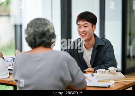 Ein glücklicher und professioneller asiatischer Architekt oder Innenarchitekt berät mit einem Kunden im Büro bei Bauplänen und Entwürfen. Stockfoto