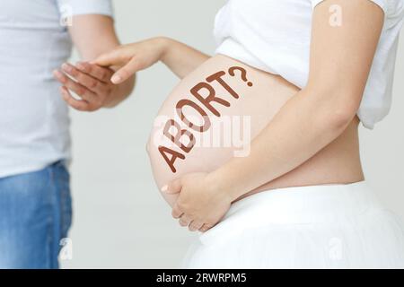 Eine schwangere Frau hält die Hand ihres Mannes auf dem Bauch mit der Inschrift - ABTREIBUNG, ein Fragezeichen. Schwangerschaftskonzept. Stockfoto