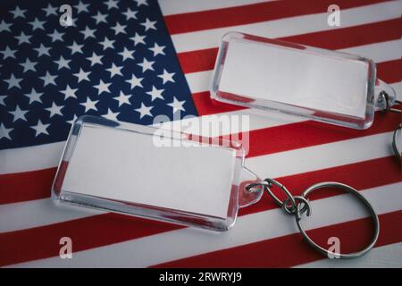 Zwei Schlüsselanhänger mit leerem weißen Etikett liegen vor dem Hintergrund der amerikanischen Flagge. Kopierbarer Bereich für ein Design oder einen Text Stockfoto