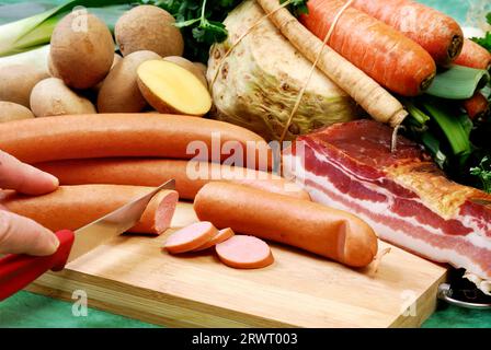 Würstchen werden auf einem Brett geschnitten. Vor frischem Gemüse und Speck angeordnet Stockfoto