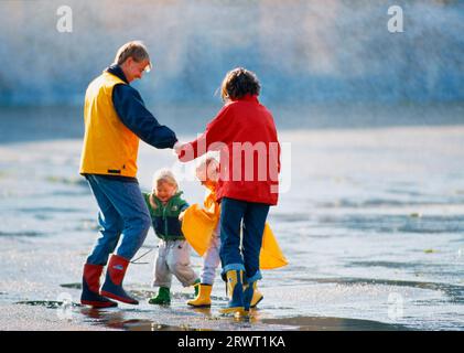 Familie mit 2 Kindern in farbenfroher Regenkleidung auf einem Spaziergang, bei dem digitale Spiele und KB-Folien gespielt werden Stockfoto