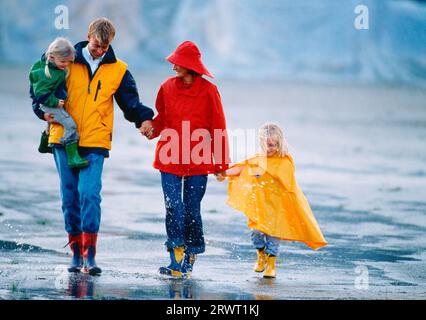 Familie mit 2 Kindern in farbenfroher Regenkleidung auf einer digitalen und KB-Rutsche Stockfoto