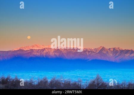 Die Hotaka-Bergkette in der Morgensonne und der Vollmond vom Takabotchi-Plateau aus gesehen Stockfoto