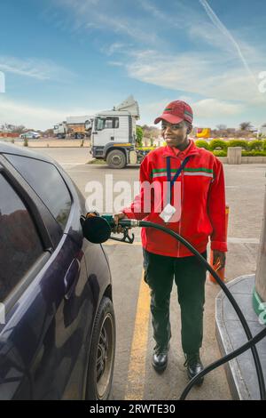 afroamerikaner in Uniform an der Tankstelle, ein kleines Auto mit Benzin befüllt, Düse im Tank Stockfoto