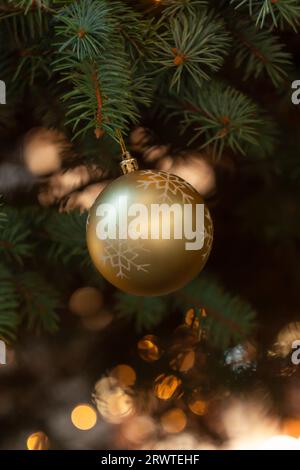Nahaufnahme der goldenen Kugel auf dem weihnachtsbaum. Bokeh-Girlanden im Hintergrund. Neujahrskonzept. Festliche Kugeln und ein Fichtenzweig, verziert mit Witze Stockfoto