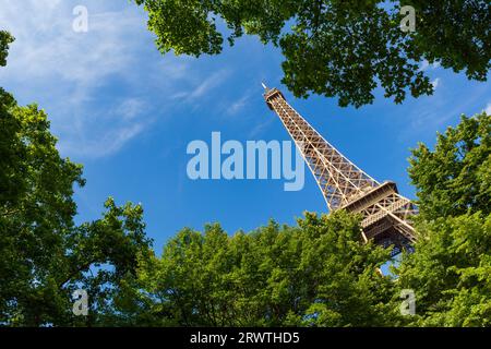 Der Eiffelturm, ein schmiedeeiserner Gitterturm auf dem Champ de Mars in Paris, Frankreich, fotografierte an einem Sommertag durch Bäume. Stockfoto