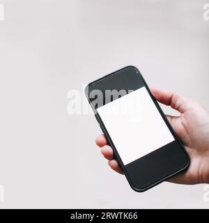 Nahaufnahme der Hand einer Frau mit einem Smartphone, das an einer weißen Wand isoliert ist. Weibliche Hand zeigt leeren Bildschirm des modernen Smartphones. Hand hält schwarzes Smartphone Stockfoto
