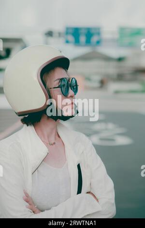 asiatische Frau, die einen Anti-Klopfhelm trägt und auf der Straßenseite der Stadt steht Stockfoto