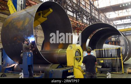 PRODUKTION - 24. August 2023, Sachsen, Leipzig: Bei der SIAG Tube&Tower GmbH arbeiten Mitarbeiter an einem Stahlrohrsegment für Windturbinen. Aufgrund der langen Genehmigungsverfahren für Schwerlasttransporte zu den Windparks und der daraus resultierenden erschöpften Lagerkapazitäten musste die Produktion in den letzten Monaten eingeschränkt werden. Derzeit hoffen die Mitarbeiter auf wesentlich kürzere Bearbeitungszeiten bei den Behörden und eine Lösung des Transportrückstands. Ziel ist es, die Produktion langsam wieder anzukurbeln und Kurzarbeit für Anlageningenieure zu vermeiden. Das Unternehmen, das einer der führenden Anbieter der Windenergie-Sekte ist Stockfoto