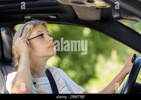 Frau, die in den Rückspiegel des Autos schaut, um Mascara aufzutragen Stockfoto