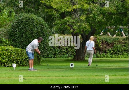 Mann und Frau mittleren Alters, vermutlich ein Paar, spielen Putting oder verrücktes Golf auf einem Gras Putting Green im Sommer in Großbritannien. Stockfoto