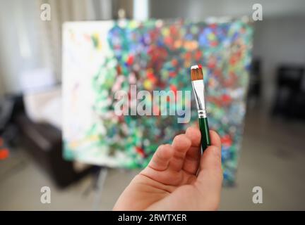 Pinsel in rot-weißer Farbe gegen Leinwand mit Bild Stockfoto
