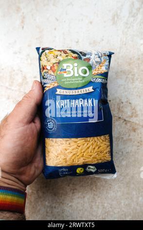 Frankfurt, Deutschland - 3. Juni 2023: Ein männlicher Mann, der ein Paket Bio-Bio-Kritharaki-Pasta über einer Steinoberfläche hält, das aus dem deutschen DM-Geschäft stammt. Stockfoto