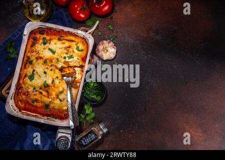 Hausgemachte Cannelloni-Pasta, großes Tablett mit gebackenen Cannelloni mit Hackfleisch mit Béchamel-Sauce, mit Kräutern in Zutaten auf dunklem Hintergrund Stockfoto