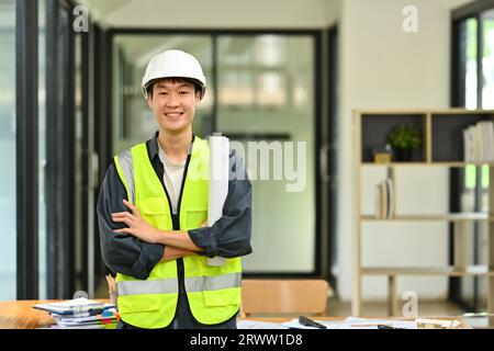 Bauingenieur mit reflektierender Weste, die mit überkreuzten Armen steht und vor der Kamera lächelt Stockfoto