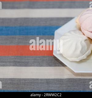 Köstlicher frischer, mehrfarbiger Luftmarshmallow liegt auf einem Serviertisch in einer Untertasse. Konzentriere dich auf weißen Marshmallow, quadratisch Stockfoto