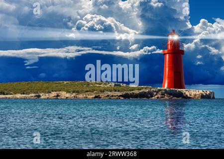 Alter roter Leuchtturm mit Lichtstrahlen an der felsigen Küste einer kleinen Insel im Meer vor einer Sturmwolke mit Regen. Fotografie. Stockfoto