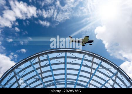 Kleines privates Propellerflugzeug, das über einem modernen Flughafen in Bewegung ist, vor einem wunderschönen klaren blauen Himmel mit Kumuluswolken und Sonnenstrahlen. Stockfoto