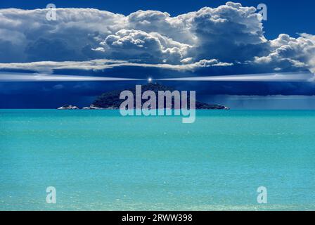 Leuchtturm mit Lichtstrahlen auf einer kleinen Insel im Meer vor einer Sturmwolke mit Regen. Fotografie. Stockfoto