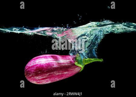 Nahaufnahme einer sizilianischen Aubergine unter Wasser mit Spritzern auf Schwarz. Stockfoto