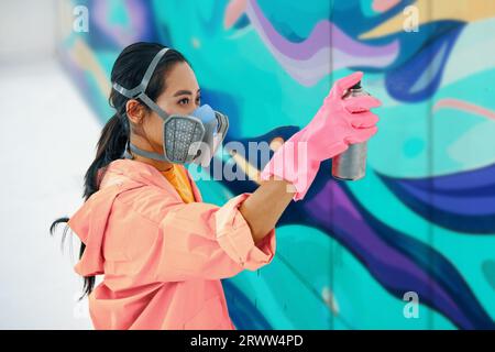 Weibliche Straßenmalerin in Atemmaske Malerei Bunte Graffiti an der Wand Moderne Kunst, städtisches Konzept. Stockfoto