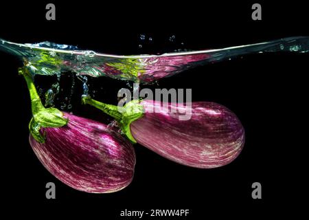 Nahaufnahme eines Paares von Graffiti-Auberginen, die mit Spritzern vor schwarzem Hintergrund in Wasser fallen. Stockfoto