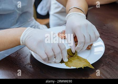 Eine Person, die Schutzhandschuhe trägt, sammelt vorsichtig ein kleines Lebensmittel: Tolma Stockfoto