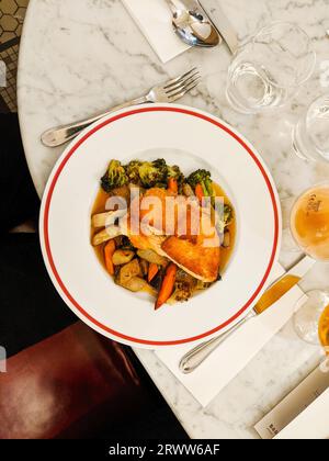 Ein weißer Teller mit einer dünnen roten Linie an den Rändern, serviert mit geröstetem Gemüse, gerösteten Kartoffeln und Fleisch auf einem Marmortisch Stockfoto