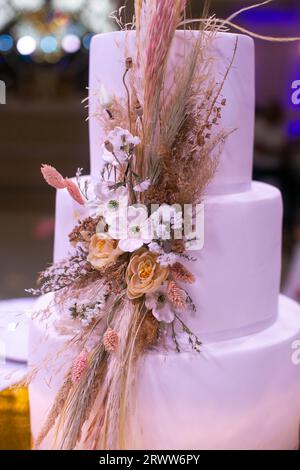 Eine elegante dreistufige weiße Hochzeitstorte mit einer wunderschönen Auswahl an wilden Blumen in einer Vielzahl von lebhaften Farben Stockfoto