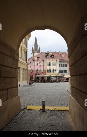 Blick durch ein Steintor, das einen Blick auf Piața Mică mit bunten Häusern (inkl. Sibiu-Auge) und Turm der lutherischen Kathedrale der Heiligen Maria in Sibiu bietet Stockfoto