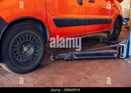 Das Rote Auto an der technischen Station bereitet sich darauf vor, auf dem Aufzug angehoben zu werden. Ein Bild des Autos in der Garage in der Nähe des Lifts. Stockfoto